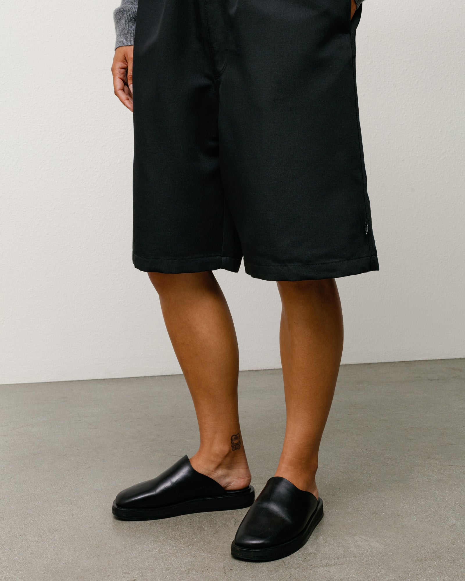 Black baggy beach shorts on model, relaxed knee-length fit with clean hem and subtle side tag.