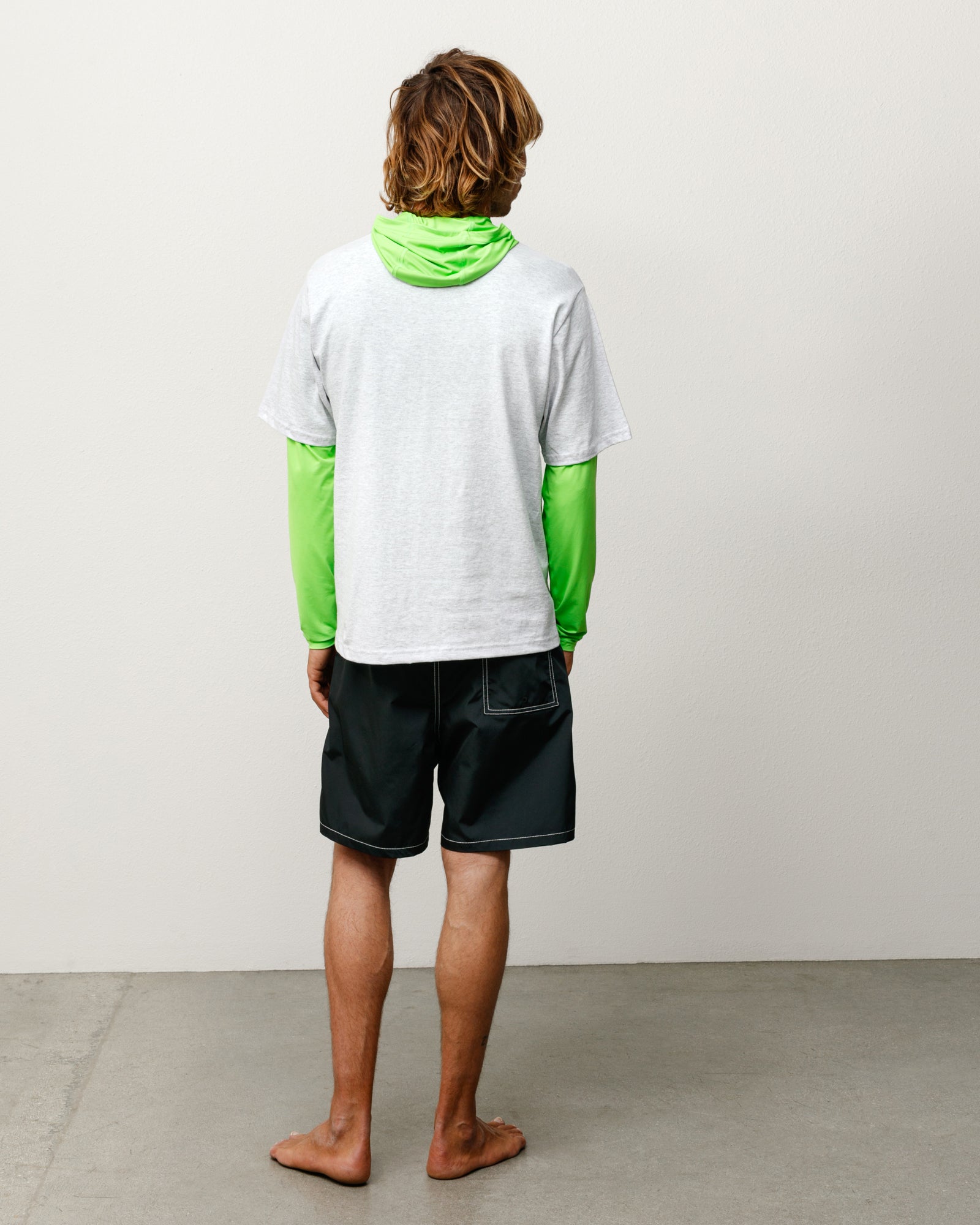 Black unisex board shorts, back view on model with rear patch pocket and contrast stitching