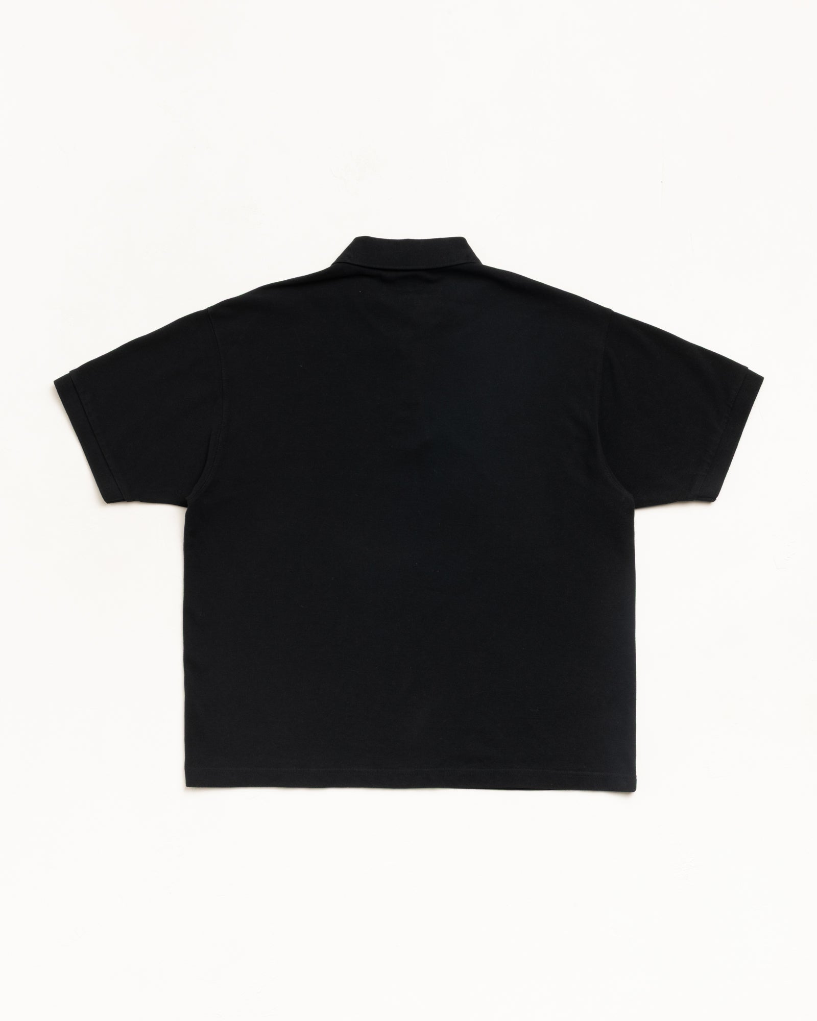 Black pique polo shirt, short sleeve, back view flat lay on white background