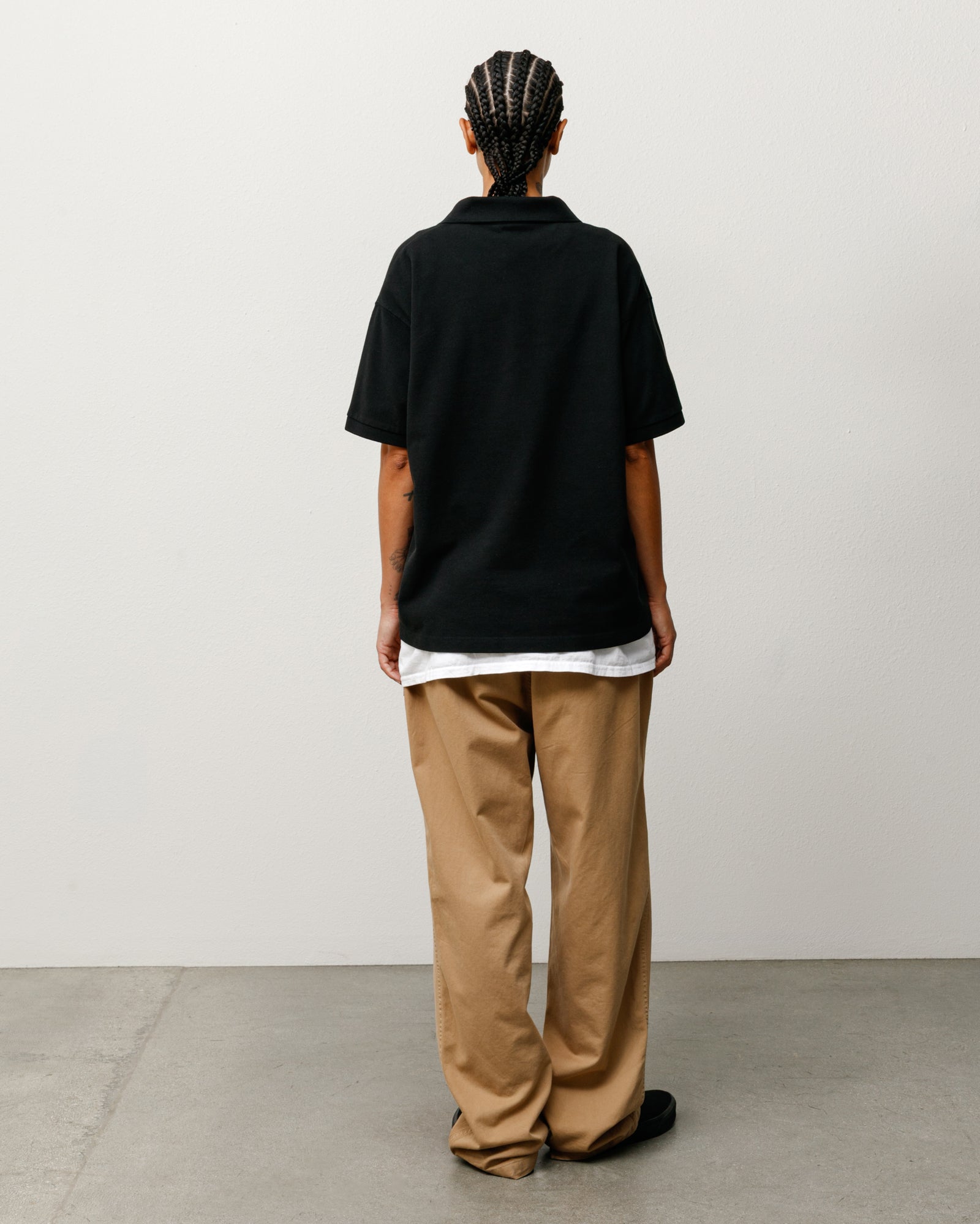 Black short-sleeve pique polo, back view on model over white tee with tan trousers