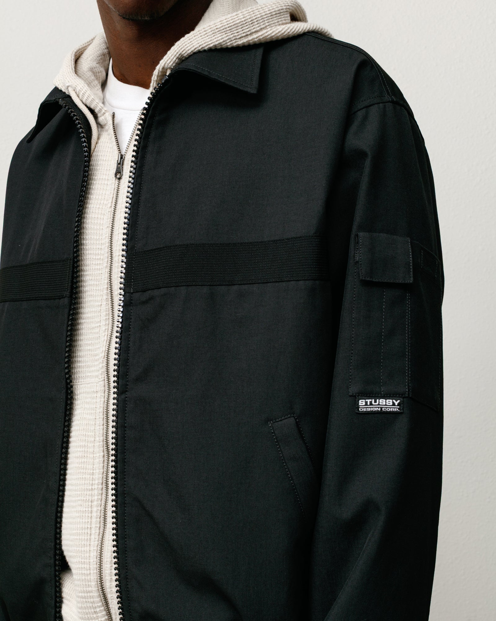 Black mechanic jacket with zip front, angled welt pockets and a sleeve patch label.