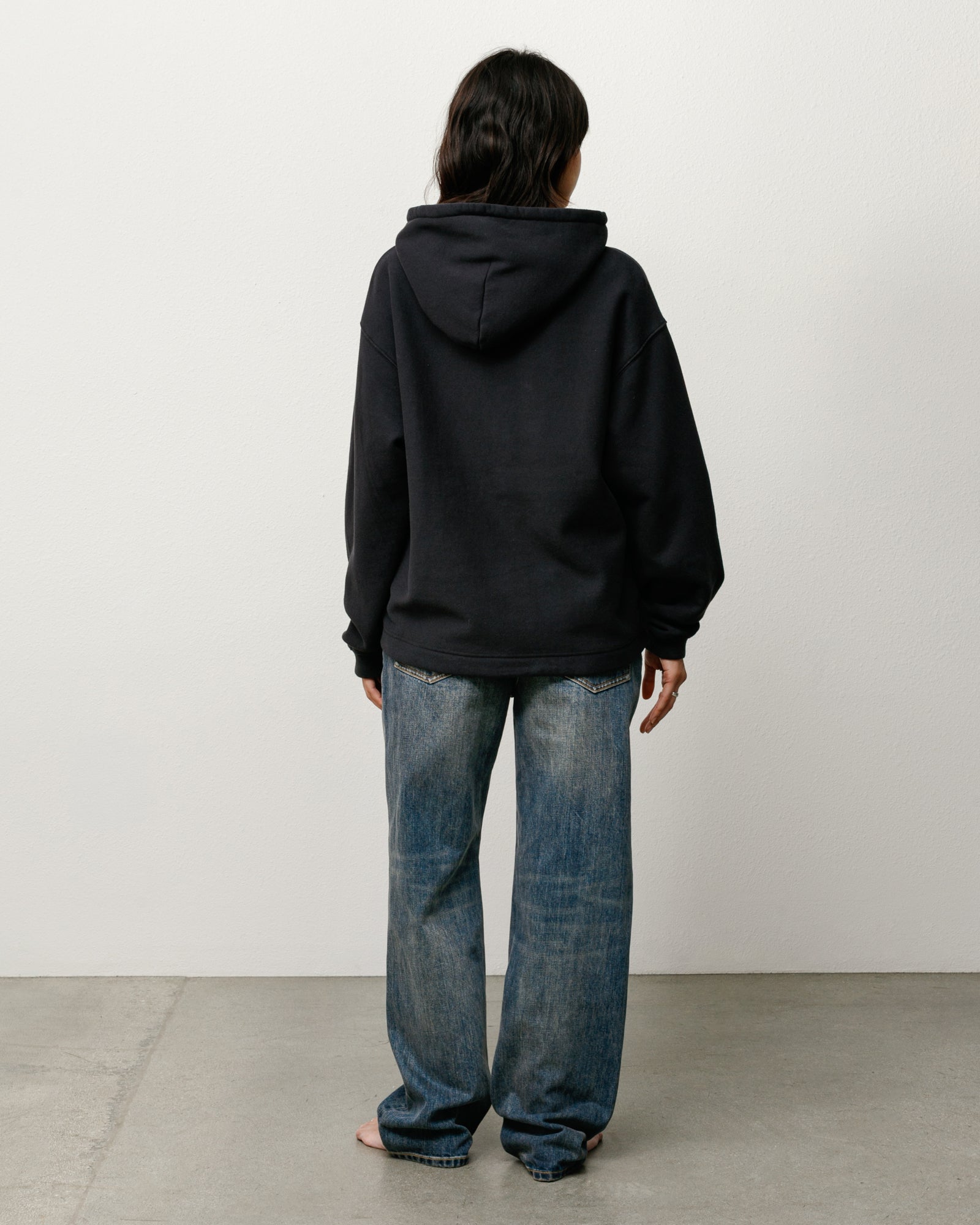 Black unisex pullover hoodie, back view on model with relaxed fit and roomy hood