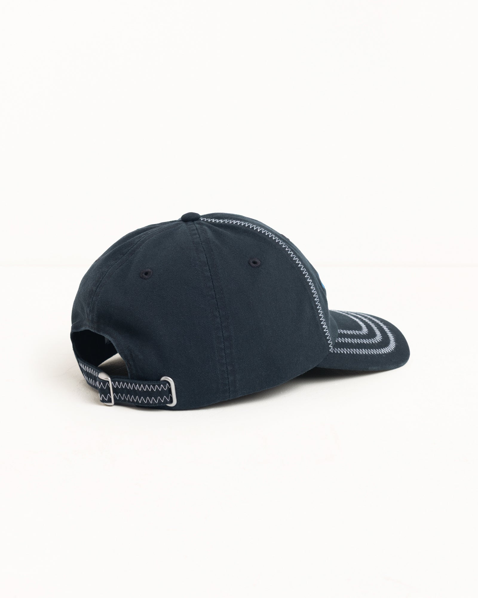 Black six-panel cap with contrast zig-zag stitching and strapback closure