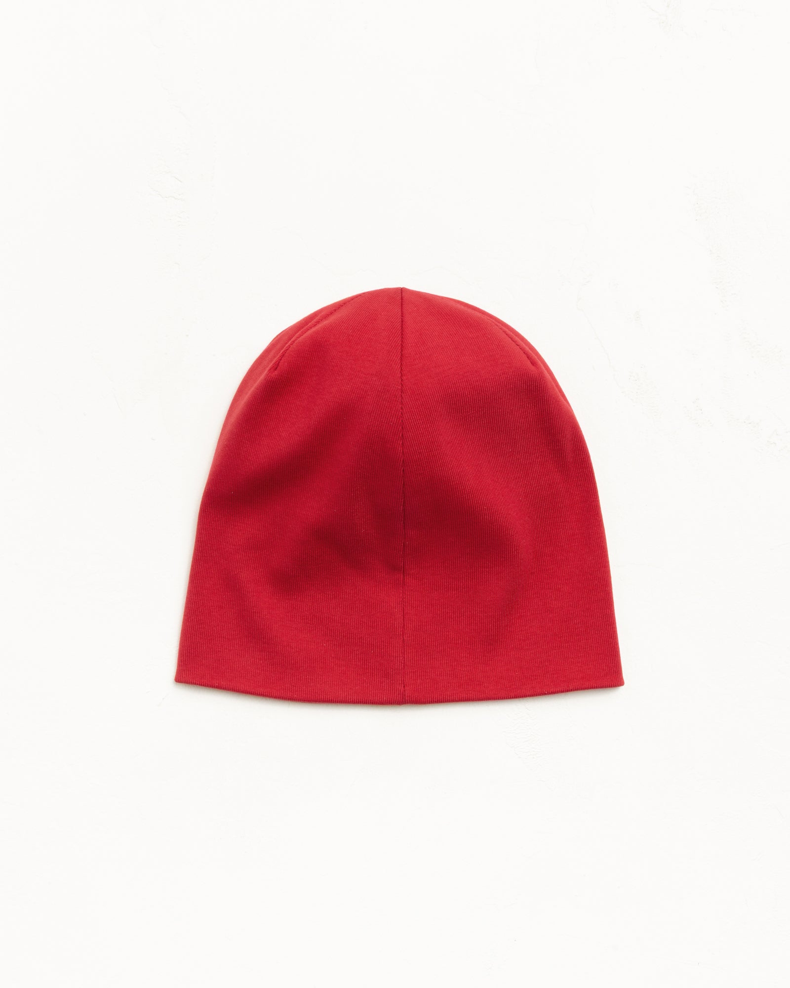 Red jersey skullcap beanie, fitted unisex, flat lay on white