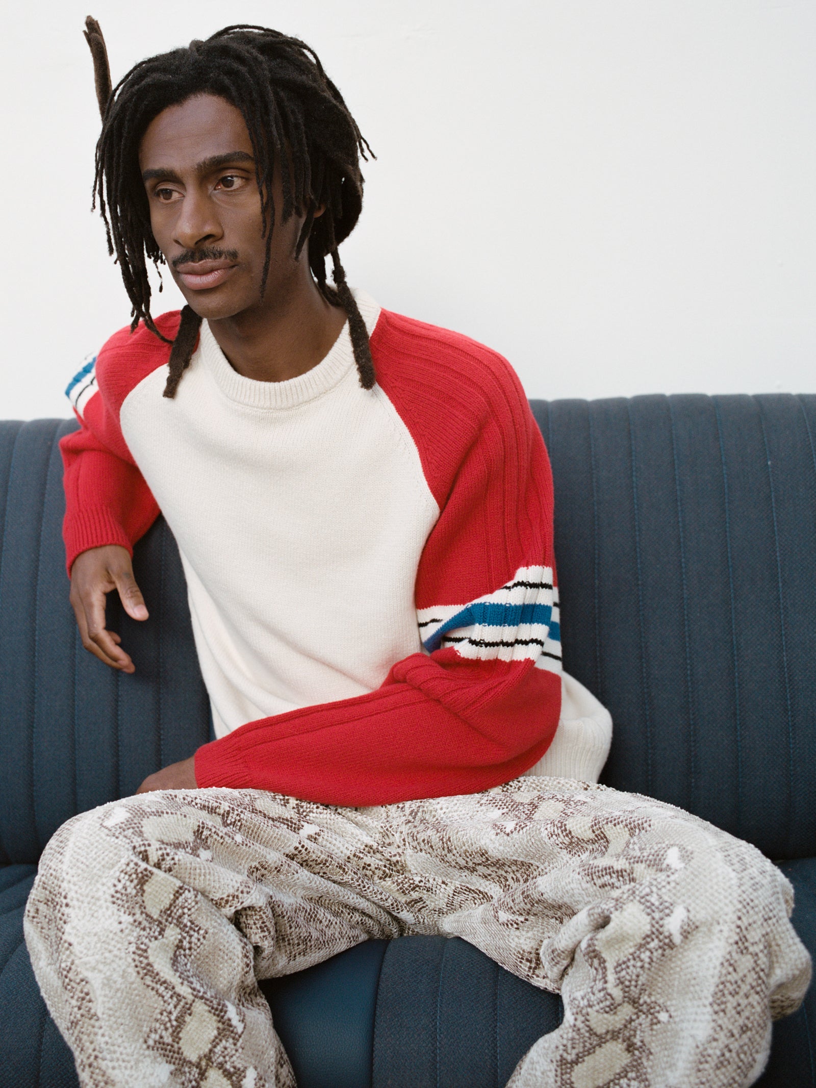 Person sitting on a blue couch wearing the Stripe Raglan Crew in Red with the New Classic Jean Python Denim.