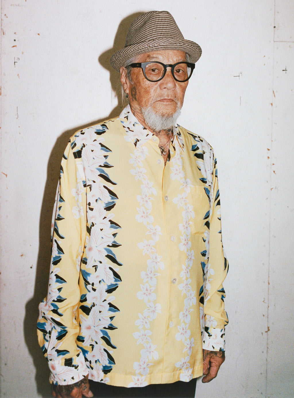 A man with glasses, a hat, and a gray beard wears the Hawaiian Floral Shirt in Yellow.
